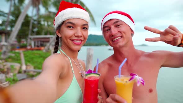 Happy Couple Smiling at Camera Taking Self-portrait Wearing Santa Hats on Beach Vacation