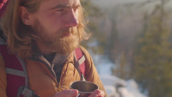 Male Tourist Drinking Hot Tea during Winter Hike in Mountains