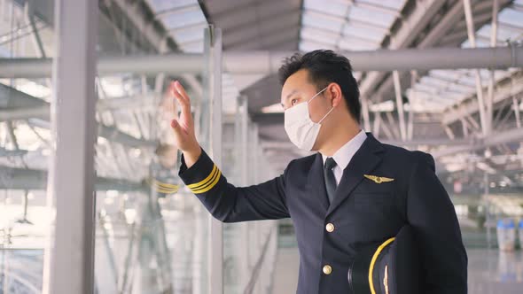 Airliner pilot wearing face mask walking in airport terminal and looking airplane with tired face.