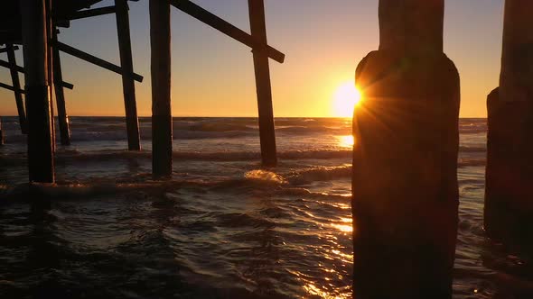 Flying under Newport Beach pier at sunset as waves roll in