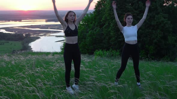 Two Young Women Doing Warm Up Exercises on the Field While Late Sunset