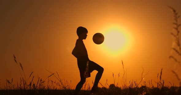 Little Boy Football Player Silhouette, Boy Juggles a Ball in the Field at Sunset