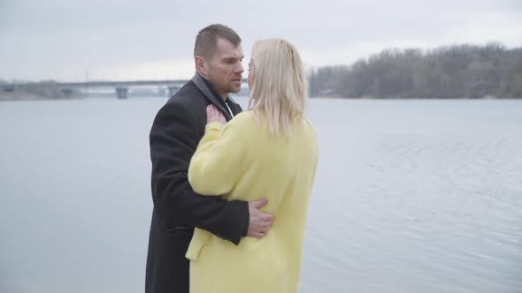 Confident Caucasian Man Spinning Blond Woman in Sensual Dance on Riverbank