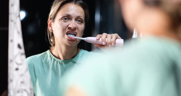 A Woman in Front Mirror Brushes Her Teeth with an Electric Brush