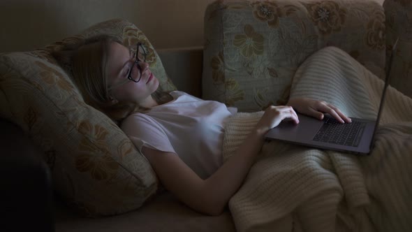 Girl Lying on a Sofa with a Laptop and Yawns Few Times, Then Falls Asleep. Night