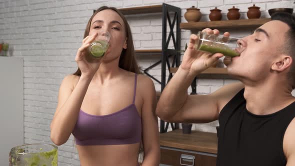 Making Green Juice at Home Young Sporty Couple in Sportswear Drinking Smoothie From a Glass