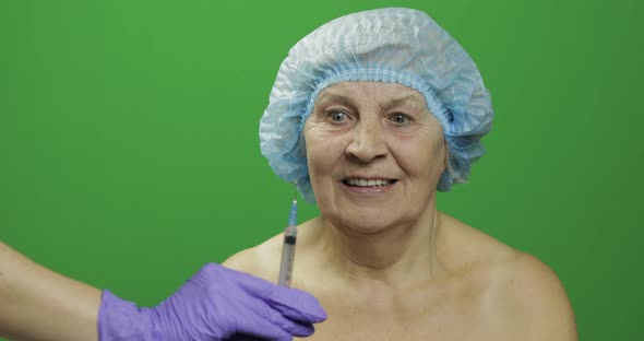 Smiling Elderly Female Lady in Protective Hat Scared of Syringe with Medicines