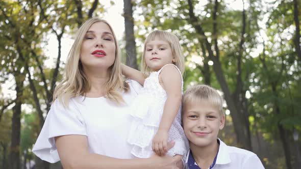 Attractive Blond Woman Holding Baby Daughter in Her Arms While Older Son Hugging Mother Smiling