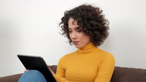 Smiling Hispanic Curly Woman Designer Uses Tablet Tapping and Scrolling Screen