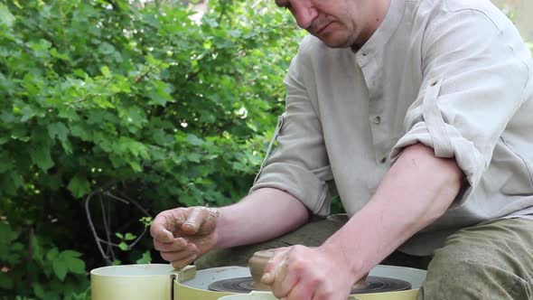 Working Gray Shirt Sculpts a Clay Pot on an Automatic Circular Machine in the Open Air