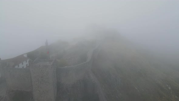 Thick fog over a medieval castle is seen by a drone flying.