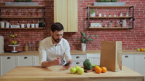 Man Browsing on Mobile Phone at Home Kitchen. Handsome Young Man Browsing on Smartphone Smiling