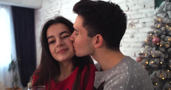 Close-up. Attractive Guy Hugging Kisses a Girl Who Is Smiling Looking at the Camera