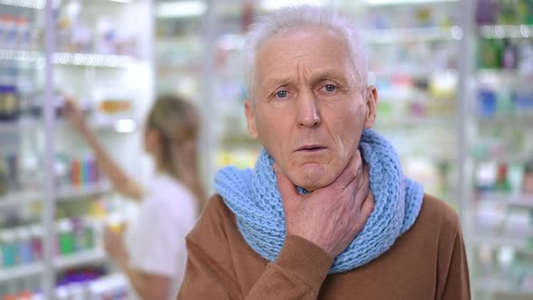Closeup Portrait of Sad Worried Senior Man Touching Painful Throat Looking at Camera with Blurred