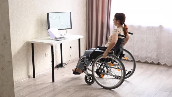 A Caucasian Woman in a Wheelchair Drives Up to Her Desk and Starts Typing with a Laptop From Home