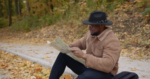 A Black Traveler Sits on the Roadside with a Map