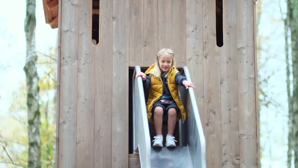 Cute Cheerful Girl at the Entrance To the Treehouse Dances and Rolls Down the Slide