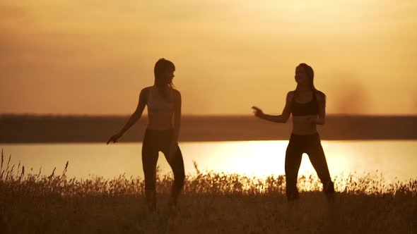 Silhouettes of Two Beautiful Girls Dancing Zumba in Field at Sunrise