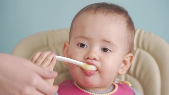 Mom teaches a newborn baby to eat food with a spoon on her own, close-up