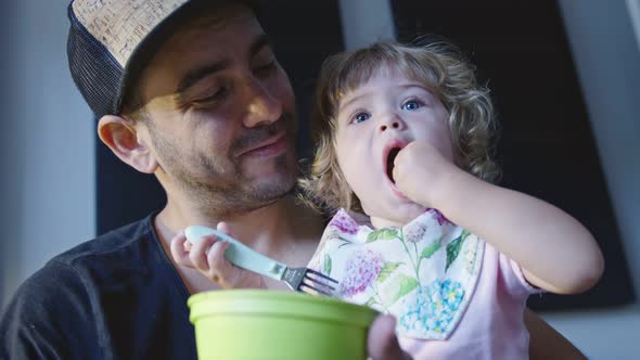 Little Girl Sitting in Father's Lap While Eating with Her Hands