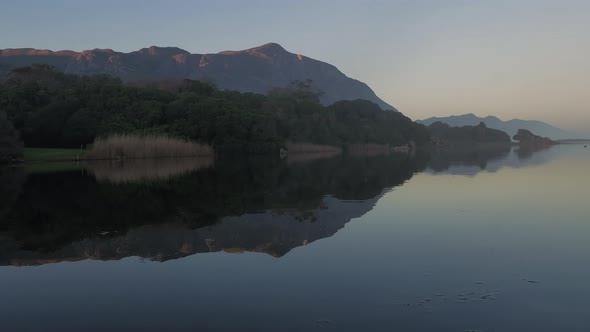 Reflection of mountain and bush on smooth surface of lagoon, tilt-up shot