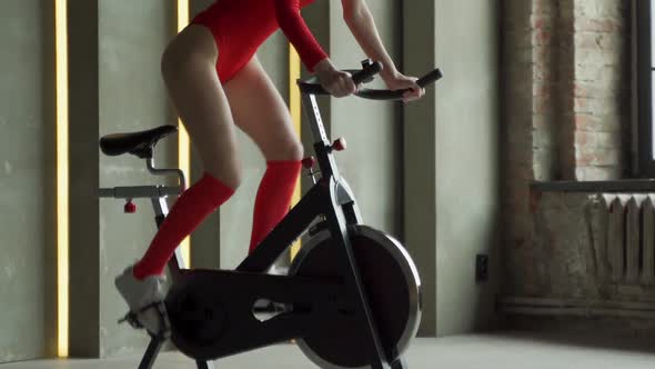 Athletic Woman in Red Bodysuit Does Aerobic Bike Workout at Gym