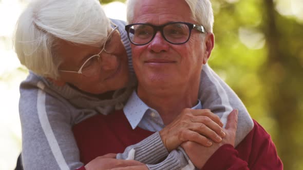 Senior Caucasian Woman Hugs Her Husband From the Back Holding Hands Together Portrait Selective