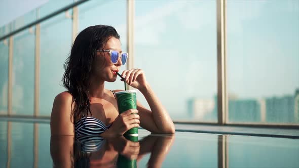 Asian American Woman in Fashion Swimsuit Drinking Nonalcoholic Orange Cocktail From Straw Relaxation