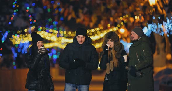 Fun Campaign of Friends Talking on the Street in the Winter. Happy Guys and Girls Drink Tea From