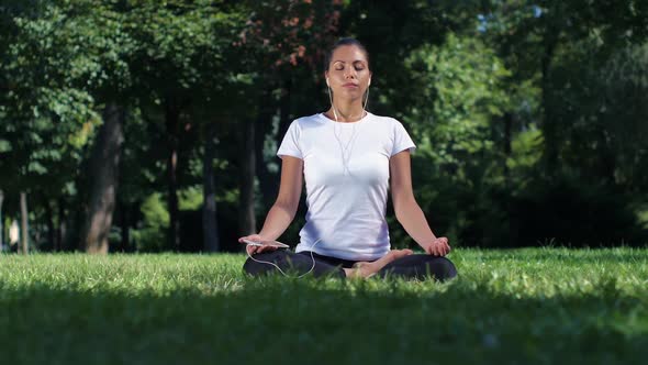 Girl Doing Yoga in the Park and Listening Music on Headphones