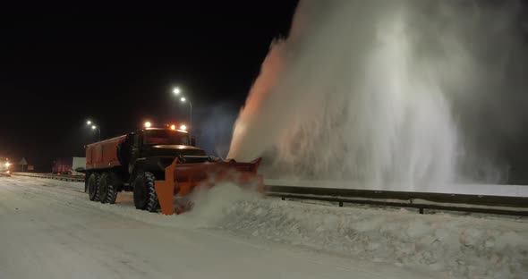 The Grader Removes Snow On The Road Outside The City At Night