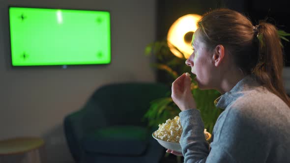 Woman Sitting on a Sofa in the Living Room in the Evening and Watching a Green TV Screen Mockup