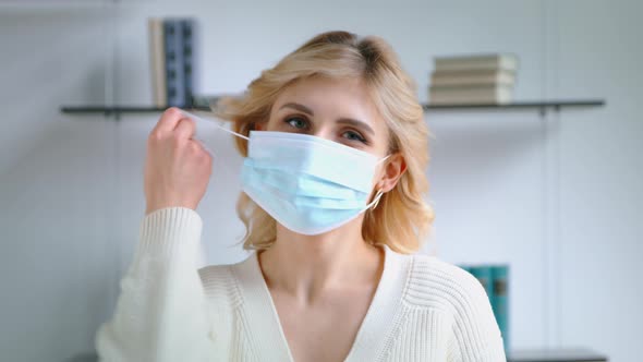 Young woman taking off medical mask and smiling while looking at camera