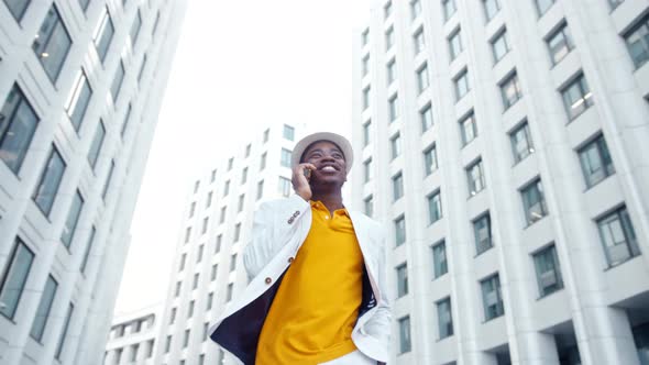 Delighted African American guy in white classic suit walks along local street