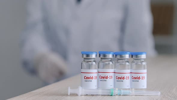 Closeup of Four Jars Bottles with Covid19 Vaccine Stand on Wooden Table in Clinic Near Syringe