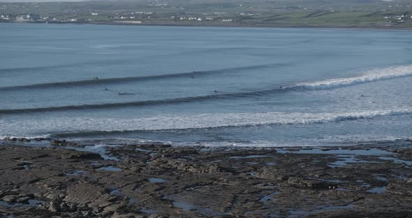 Wide shot of a coastline with surfers surfing in the water. Waves hitting the beach. Handheld camera