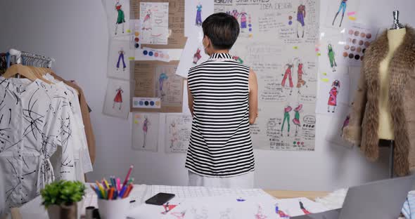 Professional fashion designer woman contemplating drawings in studio