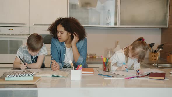 Little Students Boy and Girl Doing Homework Studying at Home with Friendly Mixed Race Nanny