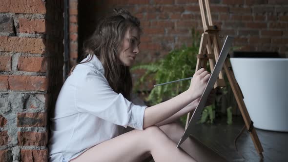 Artist Paints a Picture in a Home Studio in the Style of a Loft. Portrait of an Attractive Girl