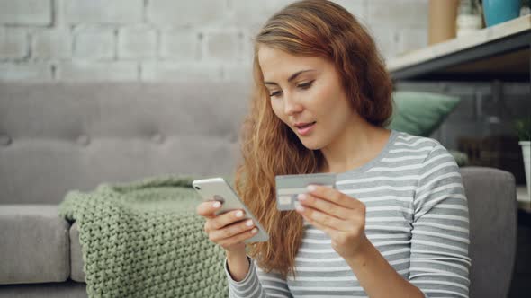 Excited Young Lady Is Making Online Payment Holding Bank Card and Touching Smartphone Screen Then