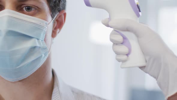 Man wearing face mask getting his temperature measured at office