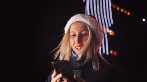 young beautiful blonde in Santa Claus hat, typing message on mobile phone