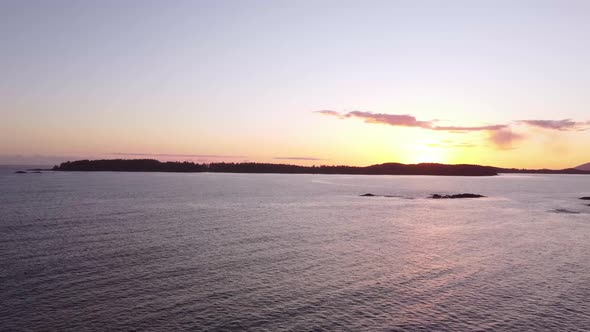 A drone video of the ocean during sunset with an island in the distance.