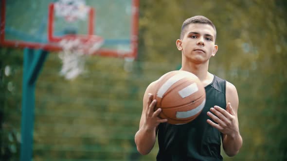 A Man Standing on a Sports Ground and Holding a Basketball Ball - Moving the Ball Between His Hands