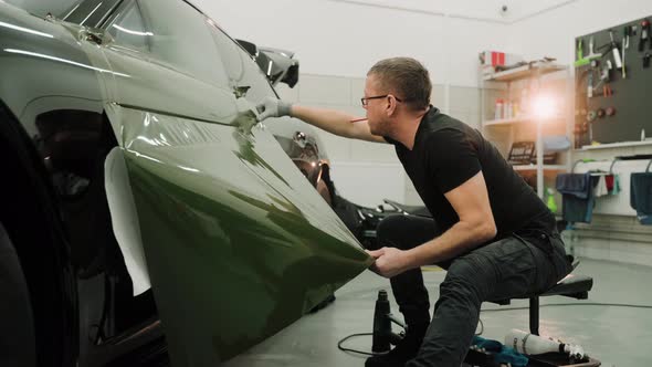 Man Pulling the Film Down While Vinyl Wrapping a Car in a Work Garage