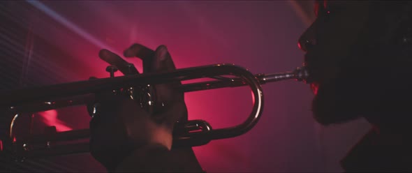Close up details of trumpeter playing in a room with bright magenta neon lights