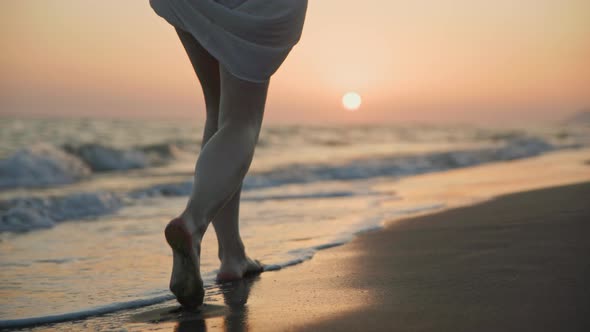 Beautiful female legs walking on the sand on the shore at sunset