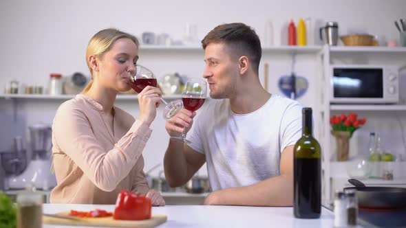 Young Couple Drinking Wine in Kitchen, Chatting and Relaxing Together, Romance