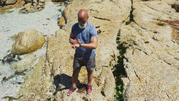 Senior african american man exercising using smartwatch on rocks by the sea