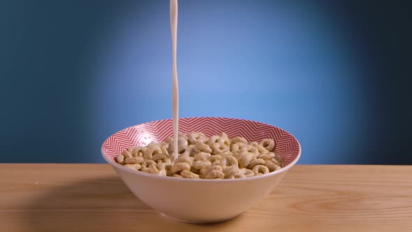 Milk is Poured Into Deep Bowl of Cornflakes in Form of Rings in Slow Motion